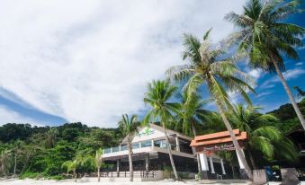 a large building is surrounded by palm trees and chairs on a sandy beach , with mountains in the background at Summer Bay Resort, Lang Tengah Island