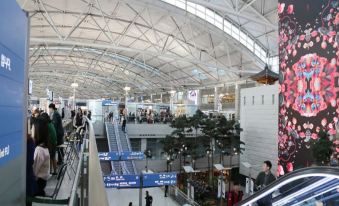 a bustling airport terminal with numerous people walking around and checking out various exhibits , including paintings on the wall at Incheon Airport Hotel