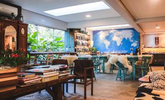 a room with wooden tables , chairs , and stools , as well as a bookshelf filled with books at Work Hotel São Leopoldo