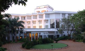 a large white hotel with a red sign and a green lawn in front of it at Sangam Hotel, Thanjavur