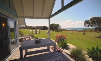 a wooden deck with a view of the ocean and a deck with chairs and a table at Bear Gully Coastal Cottages