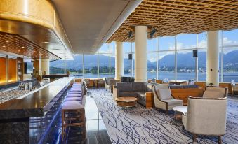 a modern bar with wooden chairs and tables , large windows , and a view of the mountains at Pan Pacific Vancouver
