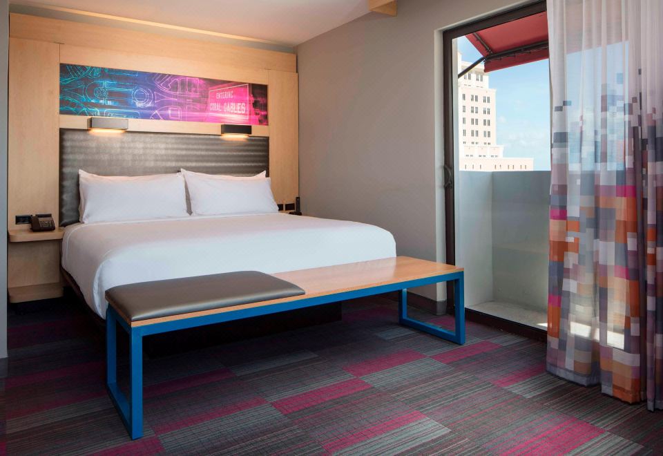 a hotel room with a large bed , a bench , and a window overlooking the city at Aloft Coral Gables