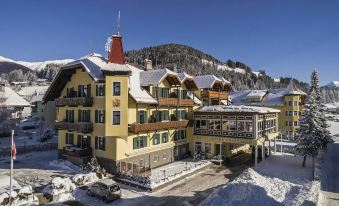 a large , yellow building with a red roof is surrounded by snow and has a car parked in front of it at Hotel Cristallo