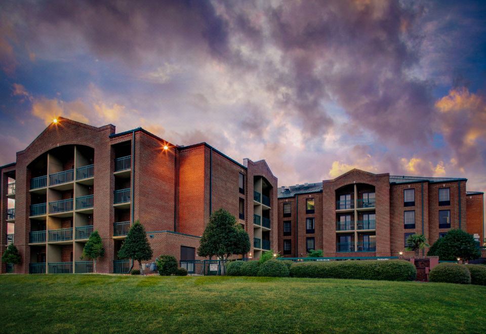 a large red brick building surrounded by a grassy area , with a cloudy sky in the background at Courtyard New Bern