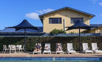 a man and a woman are sitting on lounge chairs by a swimming pool , enjoying their time together at Discovery Parks - Ballina