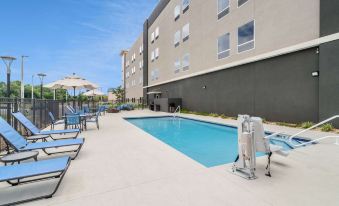 a swimming pool and surrounding area of an apartment building , with lounge chairs and umbrellas scattered around at La Quinta Inn & Suites by Wyndham Tifton