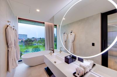 a modern bathroom with a large window , a freestanding bathtub , and two white robes hanging on the wall at Oval Hotel at Adelaide Oval, an EVT hotel