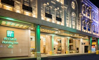 There is a building with two entrances, one of which is illuminated, and an American flag displayed at night at Holiday Inn Macau