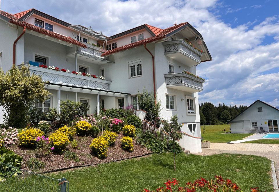 a large white house with a red roof and balconies , surrounded by a lush garden filled with colorful flowers at Frank