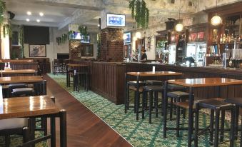 a bar with wooden tables and chairs , a television on the wall , and green carpeted floor at The Cambridge Hotel