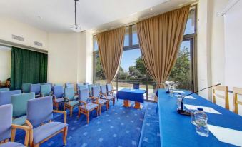 a conference room with blue chairs , a long table , and large windows overlooking the outdoors at Olympian Bay Grand Resort