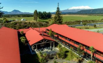 a large red building with a traditional japanese design is surrounded by lush greenery and mountains at The Park Hotel Ruapehu