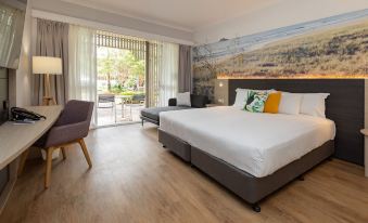 a large bed with white linens is in a room with wooden floors and chairs at Novotel Sunshine Coast Resort