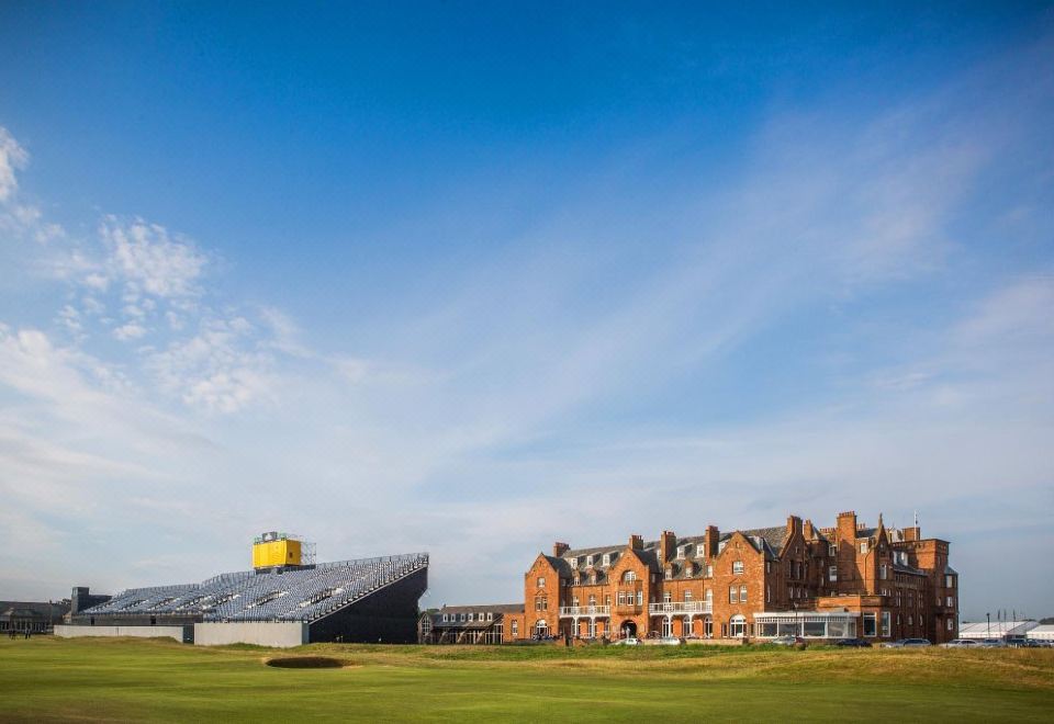 a large , orange building with a yellow logo is surrounded by a green field and blue sky at Marine Troon