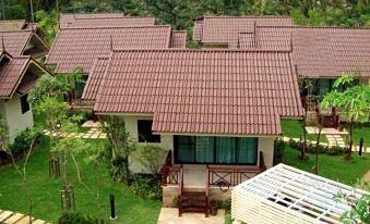 a row of small , red - tiled houses situated in a lush green environment , surrounded by trees and grass at Kuiburi Hotel & Resort