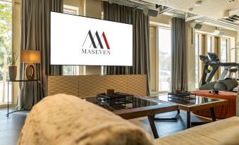 "a living room with a couch , coffee table , and a large screen displaying the words "" mackinlay "" on it" at Maseven Muenchen Messe Dornach