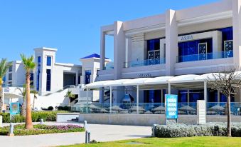 a modern white building with blue accents , situated in a sunny outdoor setting with greenery surrounding it at Pickalbatros White Beach Taghazout - Adults Friendly 16 Years Plus - Ultra All Inclusive