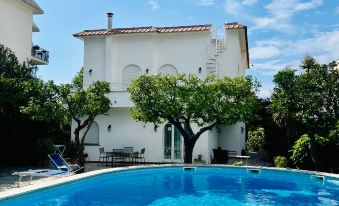 a large white house with a swimming pool in front of it , surrounded by green grass and trees at YourHome - Villa Sorrento