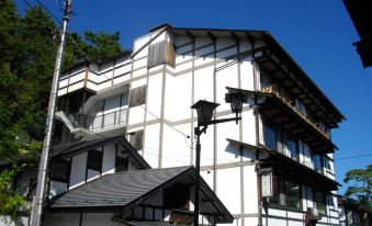 a white building with black trim and a tiled roof , situated on a street corner at Osakaya Ryokan