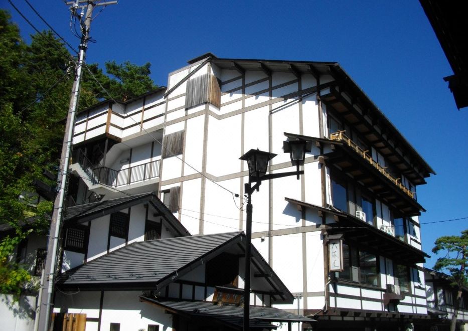 a white building with black trim , situated on a street corner under a clear blue sky at Osakaya Ryokan