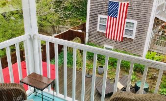 a balcony with a white railing and wooden table , overlooking an american flag painted on a red and white house at Stowaway