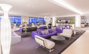 a modern lounge area with purple and white couches , chairs , and tables in a spacious room at Amfora Hvar Grand Beach Resort
