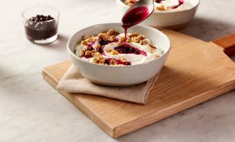 a white bowl filled with granola and topped with yogurt , accompanied by a spoon and a small bowl of jam at TownePlace Suites Grand Rapids Airport