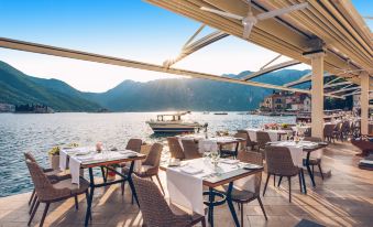 an outdoor dining area with tables and chairs set up for a meal , overlooking a body of water at Heritage Grand Perast by Rixos