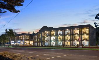 a large , modern building with multiple balconies and lights , situated on a street with trees and a clear sky at North Pier Hotel