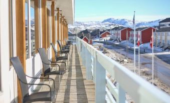 a wooden deck with several chairs and a railing overlooks a snow - covered mountain in the background at Hotel Hvide Falk