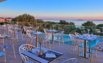 a dining area with tables and chairs set up on a rooftop overlooking a pool at Park Plaza Belvedere Medulin