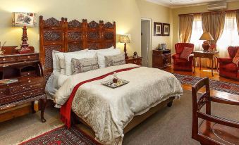 a large bed with a wooden headboard and white linens is in a room with a chair , lamp , and other furniture at Riverside Guest Lodge