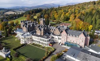 a large , historic hotel complex with multiple buildings and green spaces , situated in the heart of a mountainous landscape at Crieff Hydro