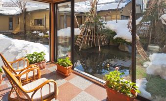 a room with a large window overlooking a pond and snow - covered ground , where several potted plants are placed at Shosenkaku Kagetsu