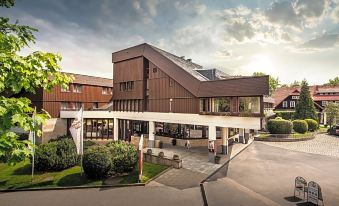 a modern building with a triangular roof and large windows , surrounded by greenery and trees at Berghotel Bastei