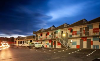 a modern , multi - story building with red and blue checkered walls , lit up at night against the dark sky at Kingston Hotel Motel