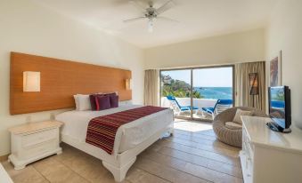 a spacious bedroom with a king - sized bed and a view of the ocean through a large window at Camino Real Zaashila Huatulco