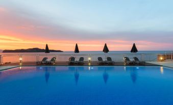 a large swimming pool with lounge chairs and umbrellas around it , overlooking the ocean at sunset at Renieris Hotel