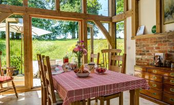 a dining table with a red and white checkered tablecloth , surrounded by chairs in a room with large windows at South Park Farm Barn