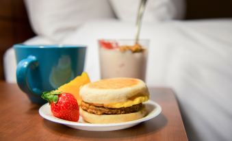 a plate with a sandwich , egg , and fruit is on a table next to a cup of coffee and a bowl of strawberries at My Place Hotel-Shakopee, MN