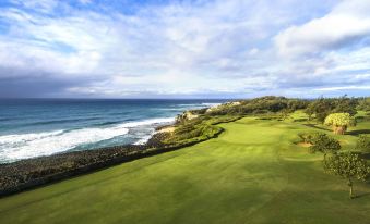 a lush green golf course with a view of the ocean in the background , under a cloudy sky at Grand Hyatt Kauai Resort and Spa