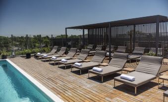 a wooden deck with several lounge chairs and towels , overlooking a swimming pool and surrounding greenery at Kos Pilar Hotel