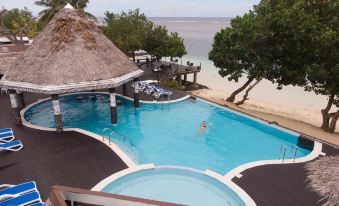 a large outdoor swimming pool surrounded by palm trees , with a beach in the background at Stevensons at Manase