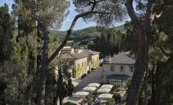 a large stone building surrounded by trees , with multiple umbrellas providing shade for the guests at Rosewood Castiglion del Bosco