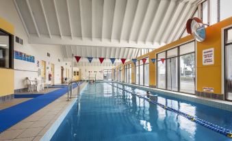 an indoor swimming pool with blue water , surrounded by white walls and equipped with a diving board at Quest Sanctuary Lakes