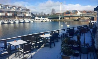 a restaurant with tables and chairs overlooking a river , boats in the water , and houses on the waterfront at Hotel Wroxham