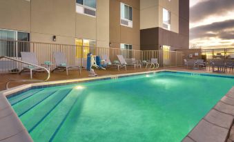 an outdoor swimming pool surrounded by chairs and umbrellas , with a building in the background at TownePlace Suites Clovis