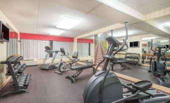a gym with various exercise equipment , including treadmills and stationary bikes , is located in a building at Ramada by Wyndham Cumberland Downtown