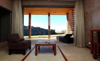 a living room with wooden furniture and a large window overlooking a beautiful landscape , including mountains at Isalo Rock Lodge